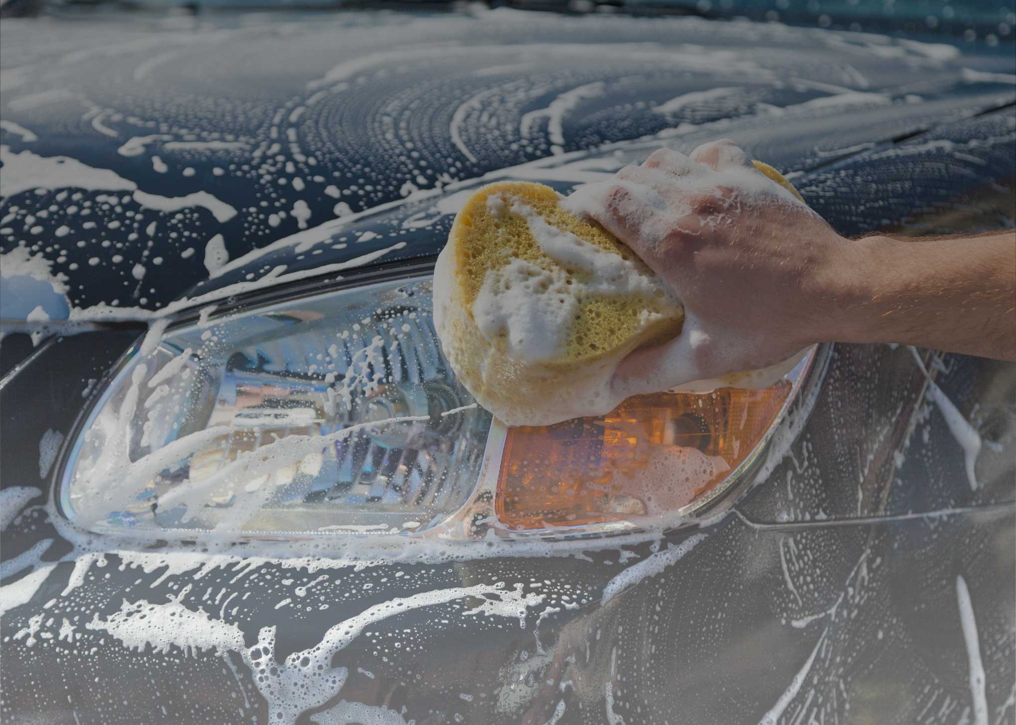 Hand washing foam off a car headlight with a sponge at A1 Auto Singh, Clyde North